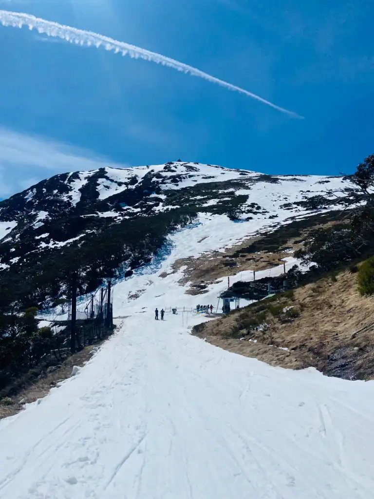 Melting snow over a ski hill as two skiers approach the lift on a sunny day.
