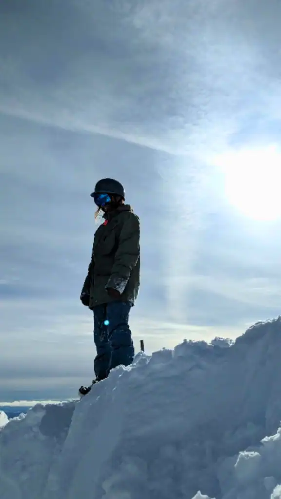 A snowboarder standing at the top off a snowy cliff ready to drop in.