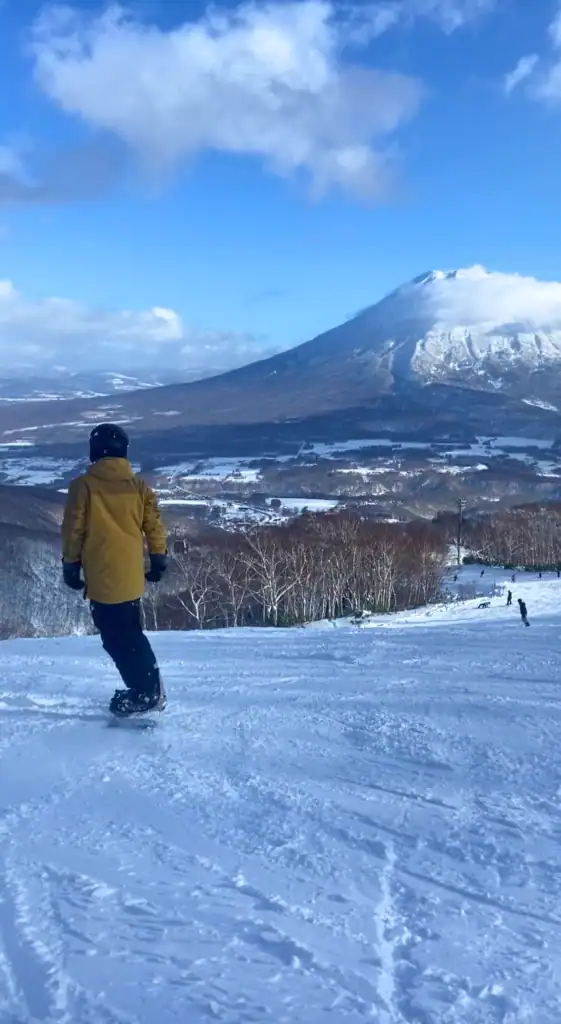 Snowboarder riding down a run on a sunny day with Mount Yotei in the background