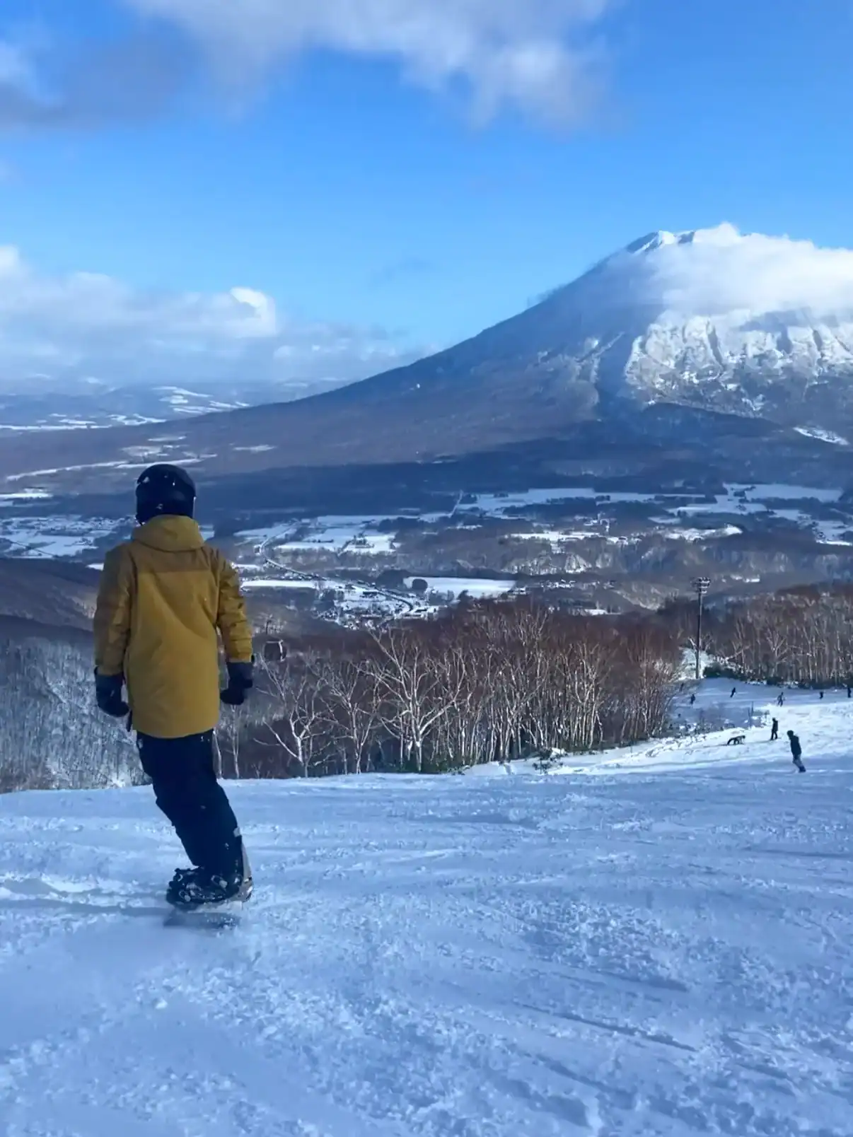 Snowboarder riding down a run on a sunny day with Mount Yotei in the background
